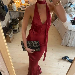 Röd balklänning - (Har även en exakt samma i pastellgul💛) Säljer en elegant röd långklänning med djup v-ringning och scarf runt halsen. Klänningen har halterneck och är ärmlös, med en figurnära passform och glansigt material som ger en lyxig känsla. Jag är 175 cm lång och brukar ha xs/s. Helt ny inga defekter. Köpt i en boutique i Frankrike