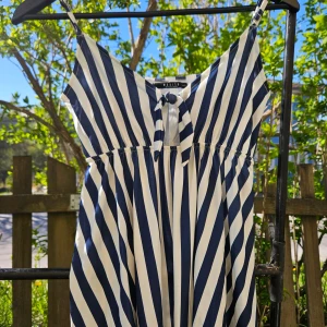 Randigt linne från Mohito - Säljer en snygg randig topp med smala axelband och knyt framtill. Toppen har marinblå och vita ränder och är perfekt för varma dagar. Lätt och luftig modell med v-ringning.