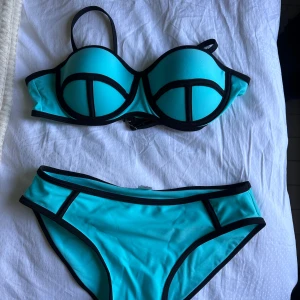 Triangl Turkos bikini med svarta kanter - Säljer denna triangl likande bikinin, helt oanvänd!!! Överdelen har bygel och vadderade kupor med en axelrem, och underdelen är midjehög. 