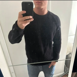 Svart stickad tröja från Weekday - Säljer en svart stickad tröja från Weekday med rund halsringning. Tröjan har en klassisk passform och är ribbstickad vid ärmslut och nederkant. Perfekt för lager-på-lager och enkel att matcha med jeans eller byxor.