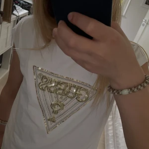 Vit ärmlös topp från Guess med paljetter - Vit ärmlös topp från Guess med glittrigt broderi. Modellen är 12 år och 153cm lång