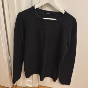 Svart stickad tröja från Size Needle - En svart stickad tröja från Size Needle i storlek M. Tröjan har rund halsringning och långa ärmar. Enkel och stilren design som passar till många olika outfits.