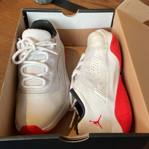 Vita och röda Air Jordan sneakers - Säljer ett par fräscha Air Jordan sneakers i vitt med röda detaljer och svart insida. Skorna har klassisk snörning, rund tå och är tillverkade i skinn och syntetmaterial.