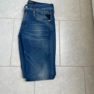 Blå Replay Anbass jeans - Säljer ett par klassiska blå Replay Anbass jeans med fem fickor och snygga slitningar. De är iprincip helt oanvända, strl 29/30