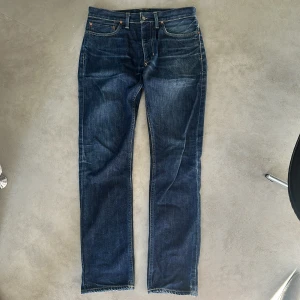 Mörkblå jeansbyxor från Polo Ralph Lauren - Klassiska mörkblå jeans från Polo Ralph Lauren med raka ben och fem fickor. Jeansen har orange sömmar och en läderpatch med logga bak i midjan. Perfekta för en stilren och tidlös look.