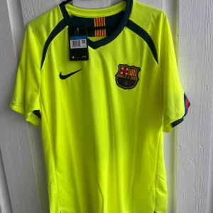 FC Barcelona bortatröja Ronaldinho 10 - Gul FC Barcelona bortatröja med Ronaldinho 10 på ryggen. Tröjan har korta ärmar, klubbmärke och Nike-logga på bröstet samt Champions League-märke på ärmen. Mörkblå detaljer vid hals och ärmslut.