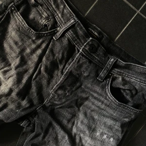 Svarta jeans från Jack & Jones - Säljer ett par svarta jeans från Jack & Jones med slitna detaljer och klassisk femficksdesign. Jeansen har normal passform och raka ben. Perfekta för en avslappnad stil.