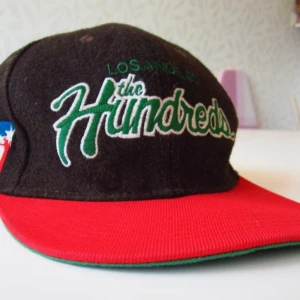 The hundreds LA keps - Keps av märket "The Hundreds" av ylle och canvas. Rengjord och enkelt lagad av mig (fäste lösa trådar i broderi). Nu i bra skick.   Justerbar storlek. Jag tror att den passar STL large till xlarge bra. 59 cm omkrets med läget på bilden. 