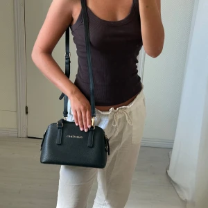 Svart handväska från Valentino - Säljer en stilren svart handväska från Valentino med gulddetaljer och struktur i skinnimitation. Väskan har både handtag och en avtagbar axelrem samt dragkedja upptill. Perfekt storlek för det viktigaste och passar till många outfits.