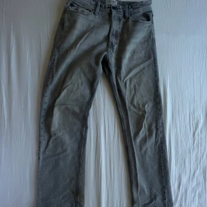 Grå jeans från Jack & Jones - Säljer ett par grå jeans från Jack & Jones med klassisk femficksdesign och raka ben. Jeansen har knappgylf och är i en stilren, ljusgrå tvätt som passar till det mesta. Perfekta för dig som gillar enkel och tidlös stil.