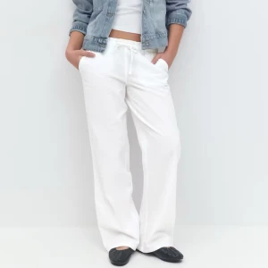 Vita linnebyxor - Säljer ett par vita linnebyxor med avslappnad passform och dragsko i midjan. Byxorna har raka, vida ben och är perfekta för en stilren och bekväm look. Passar lika bra till en enkel topp som till en jeansjacka. Observera att detta är förra årets Gina Tricot Young linnebyxor och inte årets!