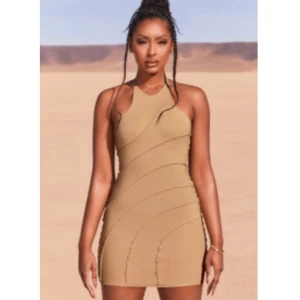 Beige kortklänning från Ohpolly - Trendig beige kortklänning med smala axelband som korsas i ryggen och asymmetriska, vågformade sömmar. Klänningen har en tight passform och är perfekt för sommarens alla tillfällen. Snygg och stilren design som framhäver figuren. Originalpris 699kr