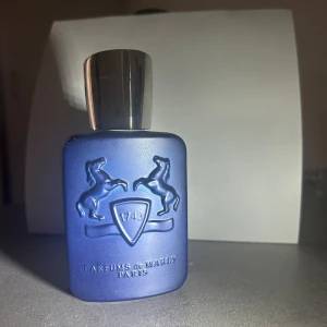 Layton Eau de Parfum från Parfums de Marly - En exklusiv parfymflaska i matt mörkblå färg med silverfärgad kork. Flaskan har två upphöjda hästar och en sköld med siffran 1743 på framsidan. Doften är Layton, Eau de Parfum, 75 ml, tillverkad i Frankrike.DET RÖDA STEÄCK VISAR HUR MYCKET SOM ÄR KVAR!!!