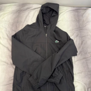 Vindjacka Lacoste - Svart vindjacka från Lacoste, använd en kort period men ser ny ut. Köptes från zalando för 1800.