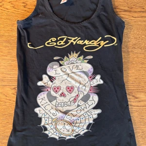 Svart Ed Hardy linnetopp med dödskalletryck - Cool svart linnetopp från Ed Hardy med stort tryck av dödskalle. Ed Hardy-tryck både fram och bak. Storleken är ordinarie XL men omsydd till en XS/S