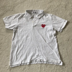 Vit pikétröja från Comme des Garçons Play - Vit pikétröja från Comme des Garçons Play med klassisk krage och knappar. På bröstet finns det ikoniska röda hjärtat med ögon broderat. Perfekt för en stilren och trendig look.
