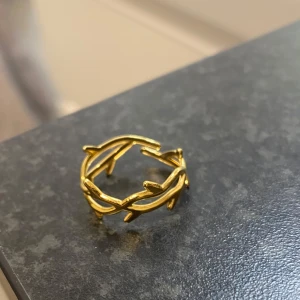 Guldring - Säljer en snygg guldfärgad ring med ett unikt bladliknande mönster. Ringen är öppen baktill och levereras i en söt rosa påse. Perfekt accessoar för att lyfta din stil!🩷🩷