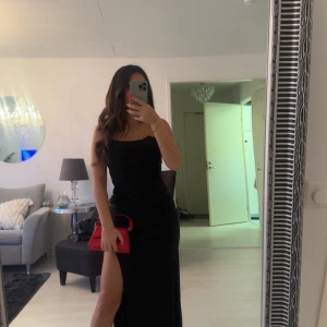 Svart långklänning med slits - Säljer en elegant svart långklänning med hög slits och axelbandslös design. Klänningen har en figurnära passform och är perfekt för speciella tillfällen. Materialet är slätt och ger en lyxig känsla. Använd en gång! 