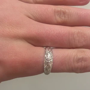 Silverfärgad ring med mönster - Säljer en snygg silverfärgad ring med ingraverat blommönster runt om. Perfekt accessoar för dig som gillar stilrena men ändå unika smycken. Passar till många olika looks! Ringen är justerbar