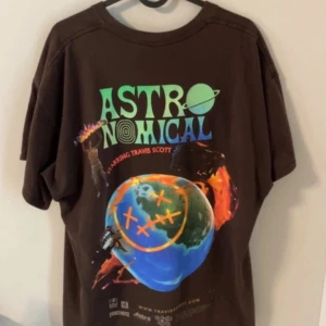 Brun Travis Scott Astroworld t-shirt - Säljer en brun t-shirt från Travis Scott Astroworld-kollektionen med färgglatt tryck på ryggen och text på bröstet. Gjord i 100% bomull och har en avslappnad passform. Perfekt för dig som gillar streetwear och unika prints.