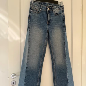 Blåa jeans med ljusare parti - Säljer ett par blå jeansbyxor i storlek XS med normal midja och raka ben . Jeansen har knappgylf och råa kanter nertill för en trendig look. Perfekta för dig som vill ha jeans till vardagen.