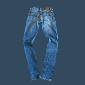 Nudie jeans - Säljer ett par klassiska blå jeansbyxor från nudie med fem fickor och snygga detaljer på bakfickan. Byxorna har normal passform och raka ben, perfekt till vardags. Ikonisk nudie baktill i midjan. W-29, modell: steady Eddie II