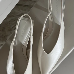 vita klackskor - Säljer ett par vita kitten heels från Stradivarius med spetsig tå och låg klack. Skorna har öppen häl med rem och är tillverkade i ett glansigt material som ger en stilren look. Perfekta för dig som vill ha bekväma snygga skor till studenten eller annat! 