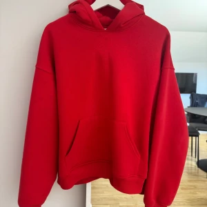 Röd hoodie med magficka - Säljer en klassisk röd hoodie med huva och stor magficka framtill. Tröjan har en avslappnad passform och är perfekt för en chill stil. Passar lika bra till jeans som till mjukisbyxor.