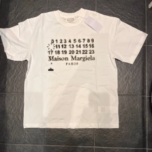 Vit t-shirt från Maison Margiela med pixeltryck - Vit t-shirt från Maison Margiela med unikt svart pixeltryck och siffror samt logga på bröstet. Klassisk rund halsringning och normal passform. Tillverkad i mjuk bomull för en skön känsla.
