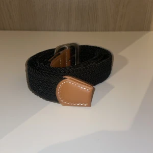 Svart flätat bälte med bruna skinn-detaljer - Snyggt svart flätat bälte med bruna skinn-detaljer och silverfärgat spänne. 85 cm. Aldrig använt.