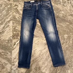 Replay Anbass Hyperflex jeans blå - Säljer ett par blå Replay Anbass Hyperflex jeans i slim fit med snygga slitningar och klassisk femficksdesign. Jeansen har normal midja och raka ben, perfekta för en stilren vardagslook. Jeansen är i stretch 