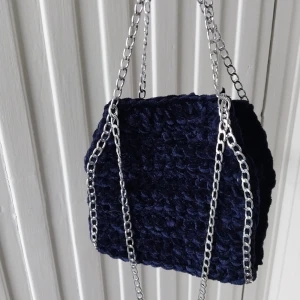 Mörkblå virkad handväska med silverkedja - Säljer en mörkblå virkad väska med grov silverfärgad kedja. Väskan har en mjuk och fluffig struktur och är perfekt för att ge din outfit en unik touch. Enkel och stilren design.