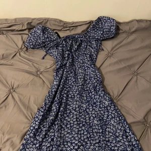 Blommig långklänning med puffärmar - Säljer en marinblå långklänning med vitt blommigt mönster. Klänningen har korta puffärmar och en smickrande v-ringning. Perfekt för sommarens alla tillfällen! Materialet känns lätt och luftigt.