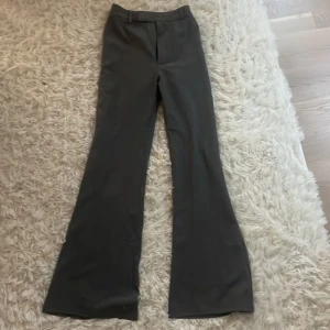 svart/grå bootcut kostymbyxor - Snygga svarta kostymbyxor med bootcut passform och klassiska pressveck. Byxorna har hällor för bälte och en diskret bakficka. Perfekta för en clean och stilren look. Materialet känns mjukt och har en lätt glans. Vet inte exakt storleken på dem då lappen är av. Men skulle säga att de sitter som storlek 32 eller 34