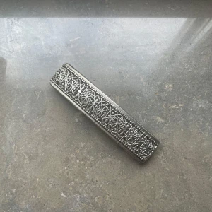 Silvrig hårklämma med mönster - En stilren silvrig hårklämma i metall med detaljerat, graverat blommönster och små hjärtan längs hela ovansidan. Perfekt accessoar för att lyfta din frisyr med en vintagekänsla och snygg detalj.