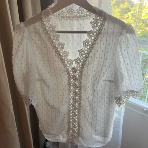 Vit blus med spets och liten puffärm - Söt blus med v-ringning, puffiga korta ärmar och  spetsdetaljer längs halsringning och ärmslut. Står ingen storlek eller vad det är för märke. Är som en XS/S