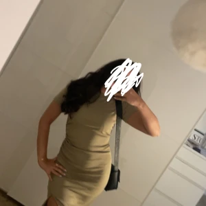 Beige tight långklänning med slits - Snygg beige långklänning med tight passform och korta ärmar. Klänningen har en enkel design med rund halsringning och en slits framtill som ger en extra edge. Perfekt för dig som gillar stilrena och trendiga plagg.