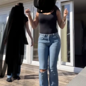 Blå jeans med hål - Säljer ett par blåa jeans med snygg slitning på ena knät. Jeansen har klassisk femficksmodell, raka ben och normal passform. De är midwaist och tillverkade i mjukt bomullstyg med lite stretch för extra komfort.
