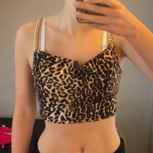 Leopardmönstrad croppad topp med kedjor - Snygg croppad topp med leopardmönster och guldfärgade kedjor som axelband. Toppens material är glansigt och har en figurnära passform. 🤎💛