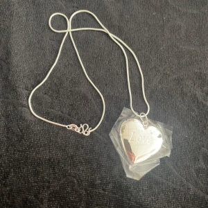 925 Silverpläterad Halsband med hjärtberlock  - Snyggt halsband i äkta silver med en hjärtformad medaljong där det står 'Love' ingraverat. Kedjan är tunn och smidig med ett klassiskt lås. Perfekt för att lägga in ett litet foto eller minne i berlocken. Stämpel 