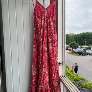 Röd blommig långklänning COCONUTMILK  - Superfin långklänning från COCONUTMILK i rött med färgglatt blommigt mönster. Klänningen har smala axelband, v-ringning och flowig passform. Perfekt för sommarens varma dagar. Är i stolek one size men skulle säga att den passar XS-S-Mbra. Inga tydliga defekter men har använts. Hör av er vid frågor!💕
