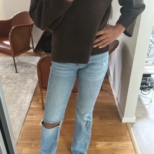 Ljusblå jeans med hål på knät - Säljer ett par ljusblå jeans med rak passform och snyggt slitage på ena knät. Jeansen har klassisk femficksdesign och är tillverkade i denim. Perfekta för en avslappnad och trendig look.