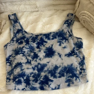 Blåvit ribbad linnetopp från SHEIN - Säljer en ribbad linnetopp från SHEIN i storlek XS. Toppen har ett snyggt blåvitt batikmönster och är ärmlös med breda axelband. Perfekt för dig som gillar en chill och trendig stil. Materialet är mjukt och stretchigt för extra komfort.