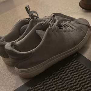 Grå mockasneakers från Selected Homme - Grå sneakers från Selected Homme i mjuk mocka med klassisk rund tå och platt vit sula. Skorna har snörning och en stilren, minimalistisk look som passar till det mesta. Perfekta för dig som gillar enkel och clean stil. Pris kan diskuteras.