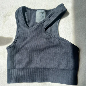 Svart ribbad topp från Aim'n - Supersnygg svart ribbad topp från Aim'n med unik design. Toppen har en croppad passform och bred resår nedtill för extra support. Perfekt för träning eller chill dagar. Stilren Aim'n-logga i metall bak.