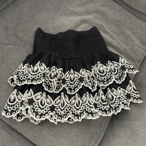 Svart volangkjol med vit broderi - Supersöt svart minikjol med bred smock i midjan och flera lager volanger. Den är från Lindex och är nåt år gammal och säljs inte längre. Skulle säga att den passar xs. 💕