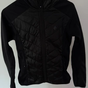 Svart quiltad jacka Cross Sportswear XS - Svart quiltad jacka från Cross Sportswear i storlek XS. Jackan har dragkedja framtill, huva och snygga diagonala sömmar på framsidan och ryggen. Perfekt för dig som gillar sportig stil och vill ha en lätt och smidig jacka med snygg passform.