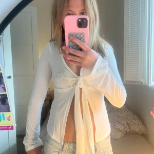 Vit omlottopp med knyt framtill - Säljer en vit långärmad omlottopp med knyt framtill. Toppen är croppad och har en djup v-ringning. Tunt och lätt material som ger en luftig känsla. Perfekt för dig som gillar trendiga och stilrena plagg med lite edge.