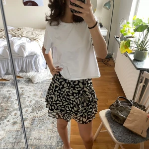 Svartvit leopardmönstrad volangkjol - Säljer en kort kjol med svart och vit leopardmönster. Kjolen har volanger och är gjord i ett lätt, luftigt material som ger en flowy känsla. Perfekt för dig som vill sticka ut med ett coolt mönster och gillar trendiga vibes.