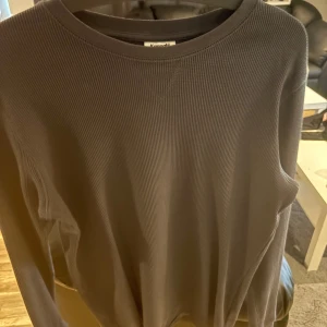 Svart ribbad långärmad tröja  - En svart långärmad tröja med ribbad struktur. Tröjan har en klassisk rund halsringning och är tillverkad i ett mjukt material som passar perfekt för lager-på-lager. Enkel och stilren design som funkar till det mesta. Är inte helt säker på storleken.